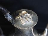 a silver tea pot with a flower on it