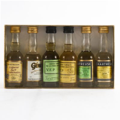 six petites bouteilles de whisky dans un coffret en bois, posées sur une surface blanche