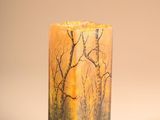 candle with a painting of trees on it sitting on a table