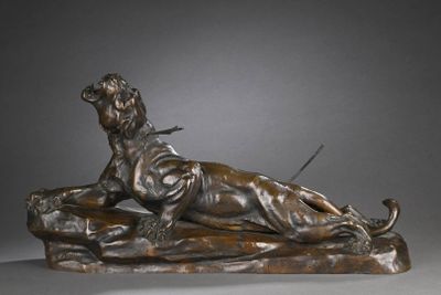 statue en bronze représentant un chien allongé sur un rocher, un bâton dans la gueule