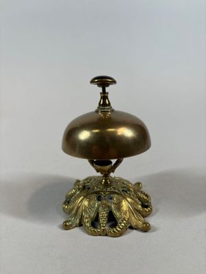 une plaque en laiton surmontée d'une cloche, posée sur une surface blanche