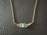 a gold necklace with a green stone on a black leather surface