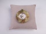 une horloge dorée et blanche posée sur un coussin, sur une surface blanche