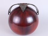 a red vase with a metal handle sitting on a white surface