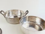 two silver bowls sitting on a table with spoons