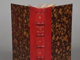 an old book with a red cover sitting on top of a table