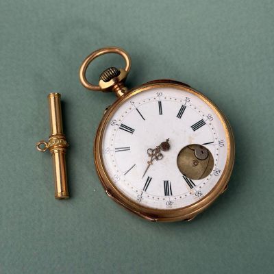 une montre de poche en or et une clé posées sur une surface verte