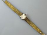 une montre en or avec un cadran blanc posée sur une surface blanche