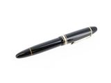 le stylo est noir avec des finitions dorées et repose sur une surface blanche