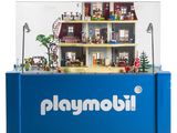 une vitrine Playmobil sur laquelle est posée une maison de poupées
