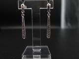 Les boucles d'oreilles sont présentées sur un présentoir transparent posé sur un socle noir