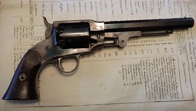 un revolver posé sur un livre dans lequel se trouve un stylo