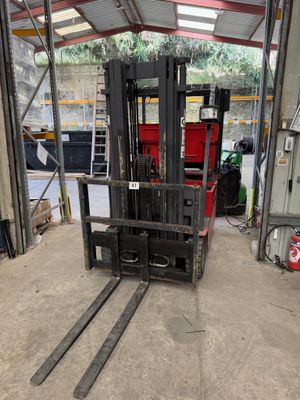 a forklift in a warehouse with a red container in the background