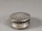 une boîte en argent contenant une pièce, posée sur une surface blanche