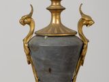 a gold and black vase on a stand with a bird on it