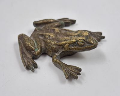 a small bronze frog sitting on a white surface