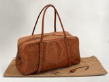 sac de voyage en cuir d'autruche marron posé sur un sac en papier marron, le tout sur fond blanc