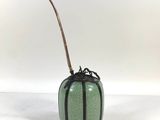 a green vase with a bamboo stick sticking out of it