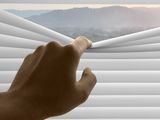 a person that is looking out of a window with blinds