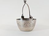 an old silver bowl hanging from a metal hook on a white background