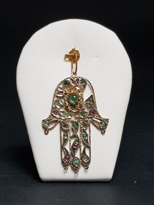 a white display case with a gold and green hamsa pendant on it