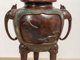 a bronze vase on a stand on a table