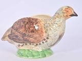 un oiseau en céramique posé sur un socle vert, sur fond blanc