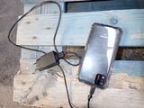 a cell phone plugged into a charger on a wooden bench