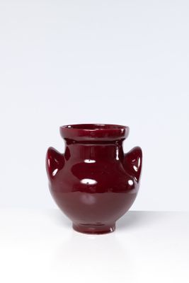 un petit vase rouge posé sur une surface blanche