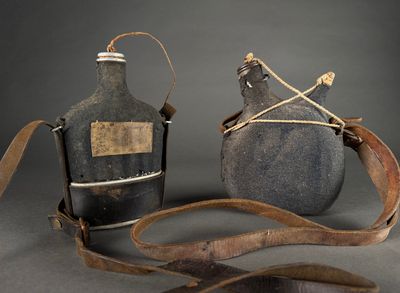 pair of antique bottles with leather straps on a gray background