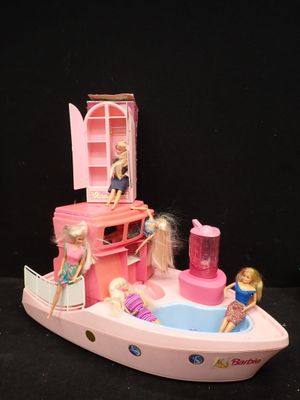 un petit bateau rose avec des poupées Barbie dessus, posé sur une surface noire