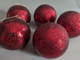 six shiny red christmas ornaments are on a table with a red ribbon