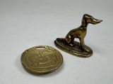 brass dog figurine next to a gold coin on a white surface