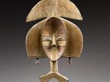 une image représentant un masque en bronze posé sur un socle en bois