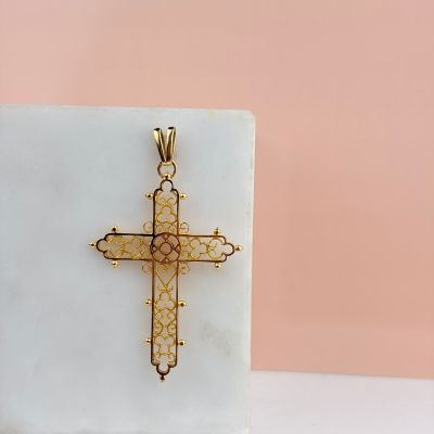 yellow gold cross pendant on a white marble block on a pink background