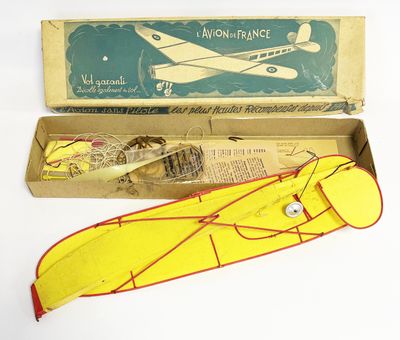 un petit avion jouet jaune et rouge dans une boîte, à côté d'un autre petit avion jouet jaune et rouge
