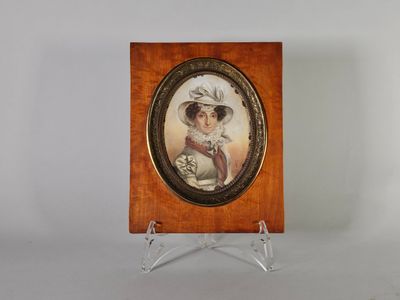 une vieille photo représentant une femme coiffée d'un chapeau et vêtue d'une robe, posée sur un socle en bois