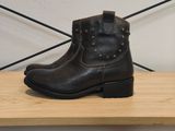 des bottes en cuir marron ornées de clous, posées sur une étagère en bois devant un mur blanc