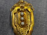 une photo d'une broche en or et perles posée sur un tissu gris