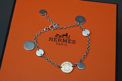 une boîte orange sur laquelle sont posés un bracelet en argent et une pièce de monnaie