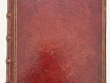 an old book with a red cover sitting on top of a white surface