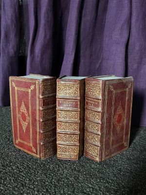 deux vieux livres posés sur une table, à côté d'un rideau violet