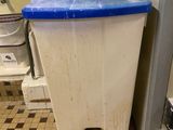 une poubelle blanche avec un couvercle bleu posée sur un sol carrelé