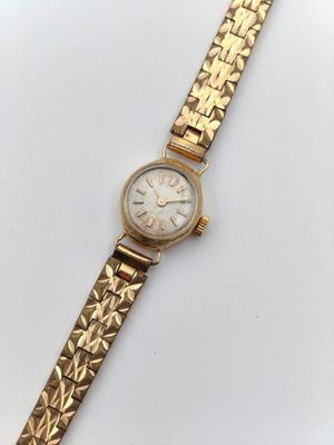 gros plan d'une montre-bracelet en or sur une surface blanche