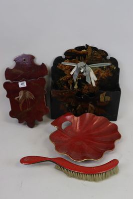 un pinceau rouge, un bol rouge et une boîte noire posés sur une surface blanche