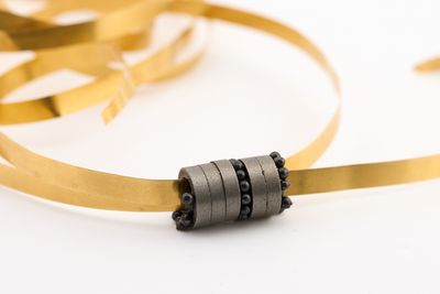 a gold ribbon and a black bead on a white surface