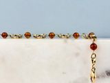 un gros plan d'un bracelet en chaîne dorée orné de perles, posé sur une surface en marbre