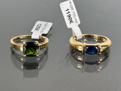 two gold rings with green and blue stones on a black surface