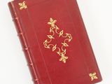 un vieux livre rouge avec des bordures dorées posé sur une surface blanche