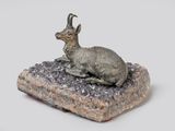 statue of a goat sitting on a rock on a white surface